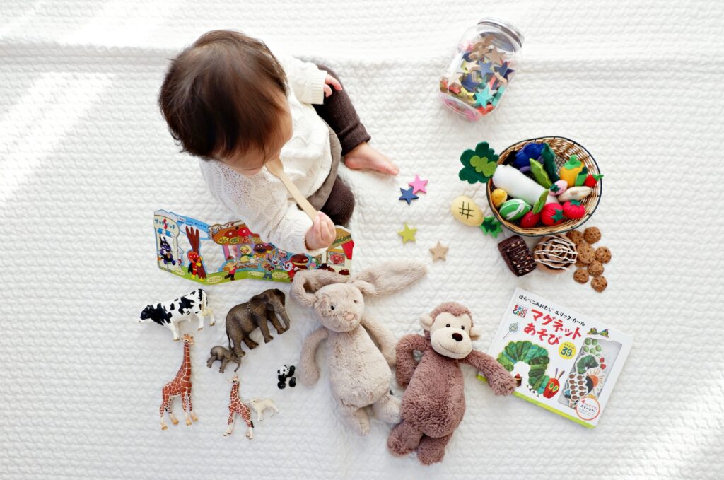 A baby sitting amongst stuffed toys and a toy bowl filled with plush-toy fruits and vegetables.