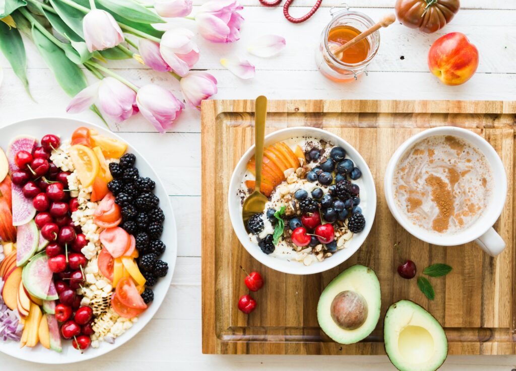 A collection of healthy breakfast options, including a big bowl of fruit, a bowl of fruit and oats, avocados, and a nectarine.